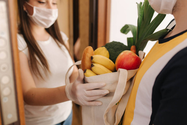 Delivery man in mask and gloves give fresh food to recipient and young woman customer. Stay home, Online shopping concept - Fotoğraf, Görsel