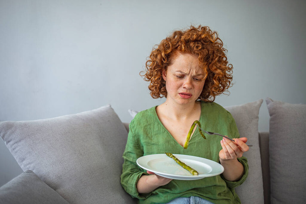 Girl keeping diet. Eating disorder. Cropped image of girl eating asparagus. Dieting habits changes. Woman hates vegetarian diet. Hungry on a diet. Displeased young woman eating green asparagus - Фото, изображение