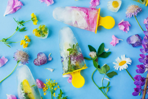 Virágos jégkrémek. Hello nyári koncepció. Fagyasztott jégkrém és jégkocka színes vadvirágokból kék háttéren lapos feküdt friss nyári virágokkal - Fotó, kép
