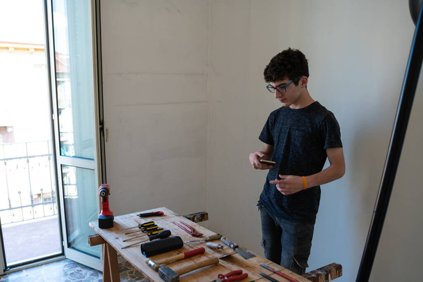 Kaukaski chłopiec zamierza zamówić narzędzia pracy na stole: śrubokręty, młoty, szczypce, nóż użytkowy i okulary ochronne widać. - Zdjęcie, obraz