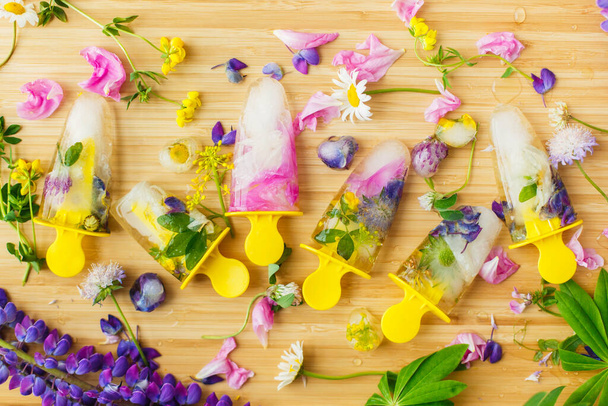 Floral Ice Pops et fleurs fraîches d'été plat laïc. Fleurs sauvages colorées dans la fonte des cœurs de glace et des glaces éclatantes sur fond en bois. Bonjour concept d'été. Image créative - Photo, image