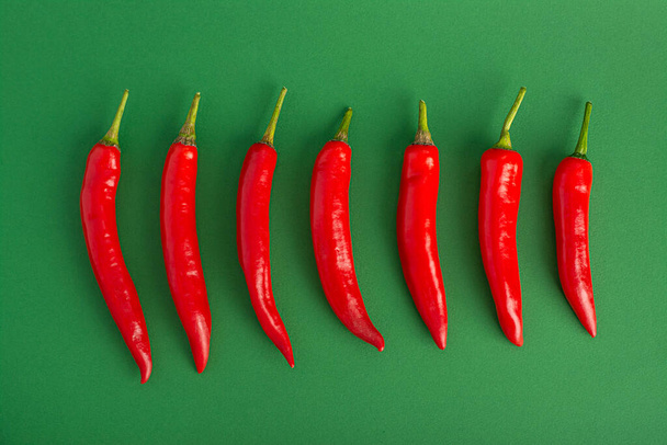 A line of red hot chili peppers on a green background - 写真・画像