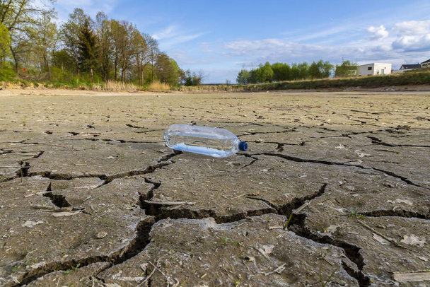 Terra incrinata con bottiglia d'acqua, metafora del cambiamento climatico e del riscaldamento globale. - Foto, immagini