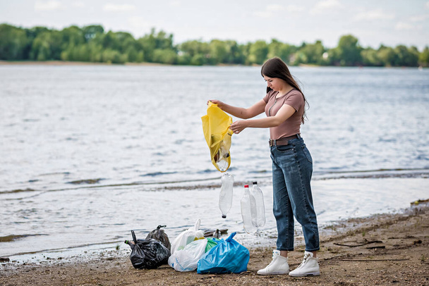 girl collects trash on the beach. girl cleans the beach of garbage - Zdjęcie, obraz