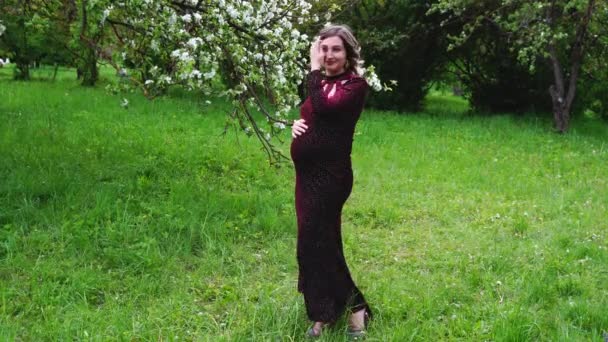 Terhes nő piros ruhában a parkban tavasszal - Felvétel, videó