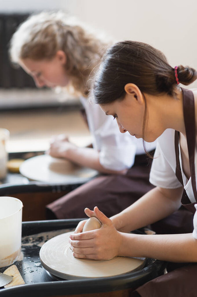 Zwei Frauen töpfern auf einer Töpferscheibe und formen Ton mit ihren Händen aus nächster Nähe. Töpferwerkstatt im Kunstatelier. - Foto, Bild