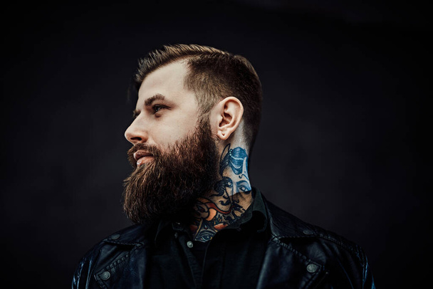 Tattooed cool bearded man in a leather jacket in a dark studio - Photo, Image