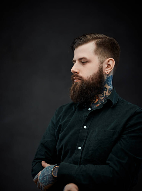 Schöner tätowierter Mann mit stylischem Haarschnitt posiert auf dunklem Hintergrund - Foto, Bild