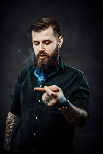 Studio portret przystojnego wytatuowanego hipstera, który pali cygaro - Zdjęcie, obraz