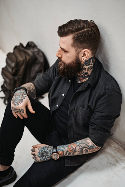 Bearded hipster guy with backpack sitting on a floor in studio - Фото, изображение