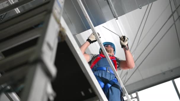 Male Worker Standing On Scaffold And Adjusting Newly Installed Air Conditioner Shaft. Holding Metal Part In Hand And Looking Down.  - Filmagem, Vídeo