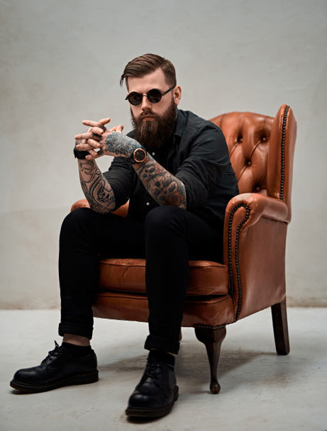Cool bearded young man sitting on a vintage chair in a studio - Photo, Image