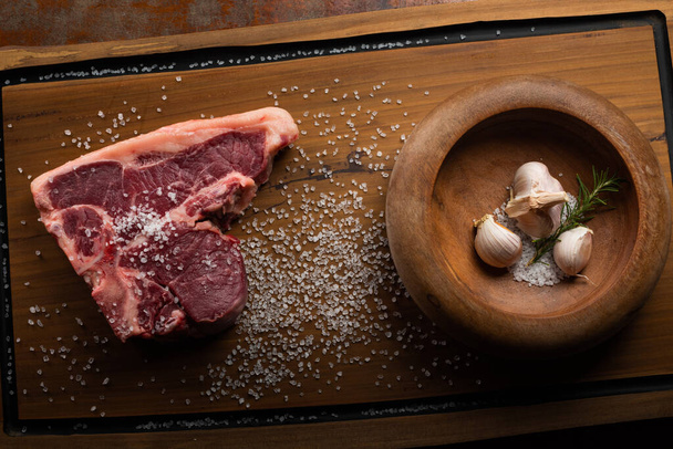 Top view raw Tibone with bone beef steak with ingredients for grilling with a spice rub, fresh rosemary and salt , on a table with dark wood texture and space for writing - Fotografie, Obrázek