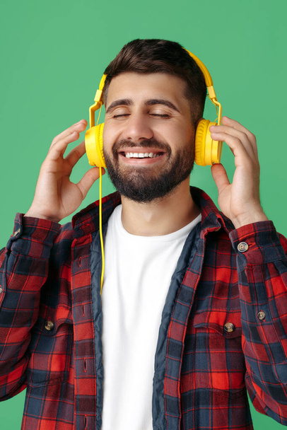 Glad bearded hipster young man in plaid shirt listening music in headphones with eyes closed over green background. - Foto, Imagem