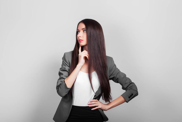 Beautiful business woman with dark hair, thinking standing on a gray background - Photo, Image