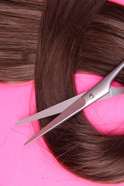 Long brown hair with scissors on pink background - Foto, afbeelding