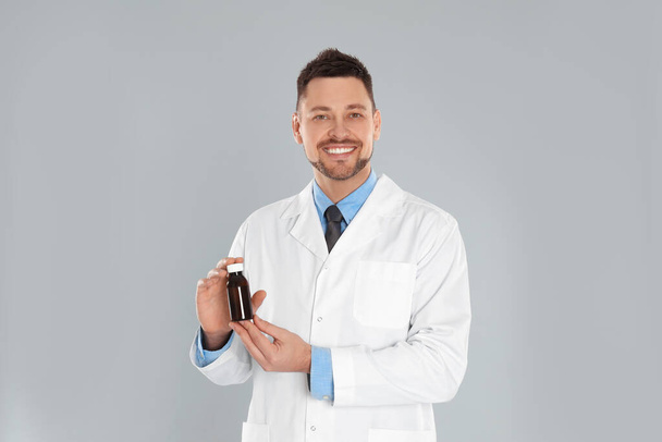 Professional pharmacist with syrup on light grey background - Foto, Imagem