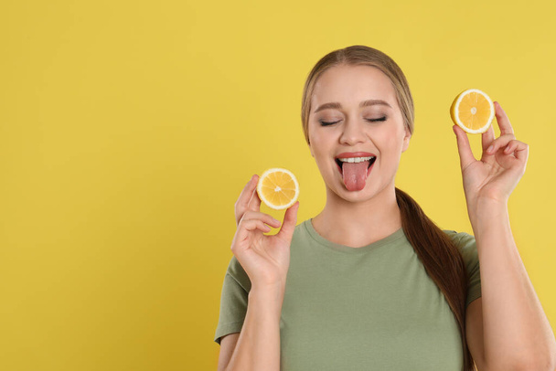 Emotional young woman with cut lemon on yellow background, space for text. Vitamin rich food - Photo, Image
