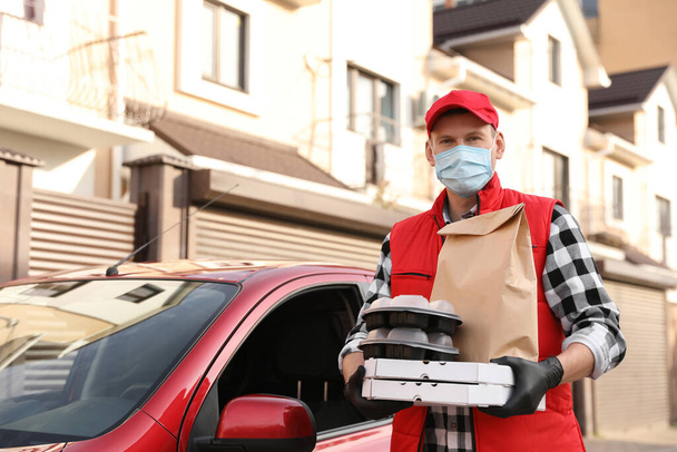 Courier in protective mask and gloves with orders near car outdoors. Food delivery service during coronavirus quarantine - Фото, изображение