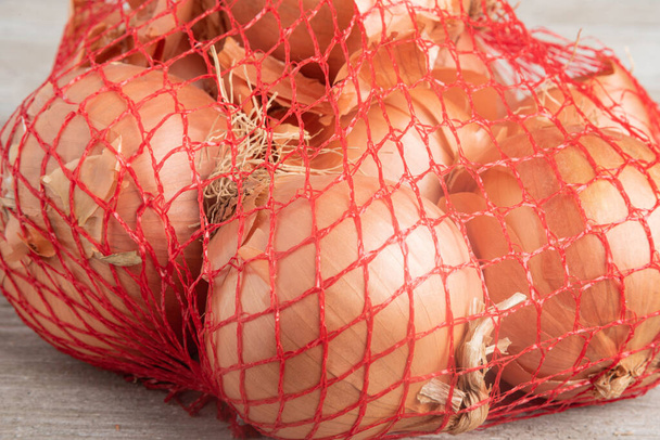 Un mazzo di cipolle confezionate in un sacchetto di rete metallica rossa flessibile per la vendita al dettaglio in drogheria e supermercati. - Foto, immagini