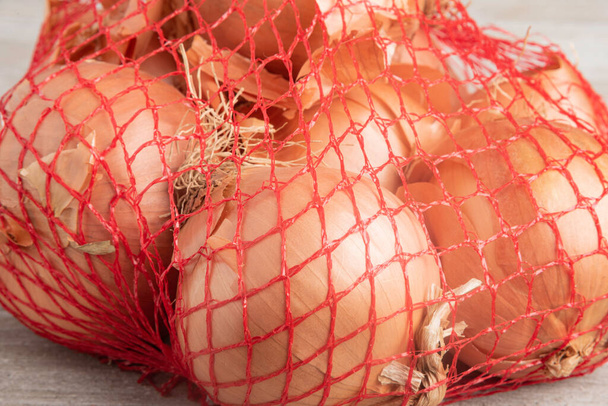 Un bouquet d'oignons emballés dans un sac flexible en treillis métallique rouge pour la vente au détail dans les épiceries et les supermarchés. - Photo, image