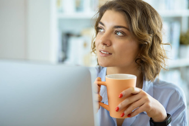 Attractive woman sitting at office desk, holding a cup of coffee - Фото, изображение