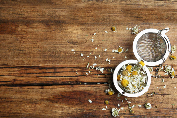 Dry chamomile flowers in infuser on wooden table, flat lay. Space for text - Fotoğraf, Görsel