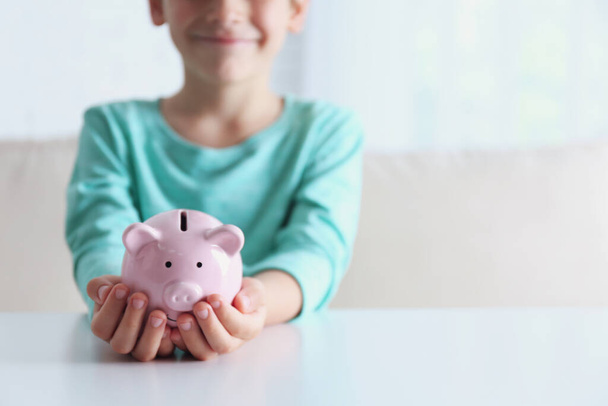 Little boy with piggy bank at white table indoors, closeup. Space for text - Fotografie, Obrázek