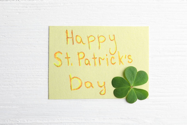 Clover leaf and note with text HAPPY ST. PATRICK'S DAY on white wooden table, flat lay - Foto, Bild