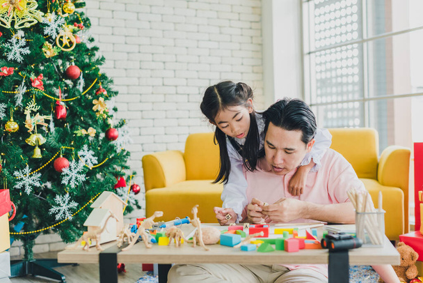 Asian father and daughter play toys on the table in the living room decorated with Christmas trees to prepare for Christmas and New Year's celebrations. - Foto, Imagem