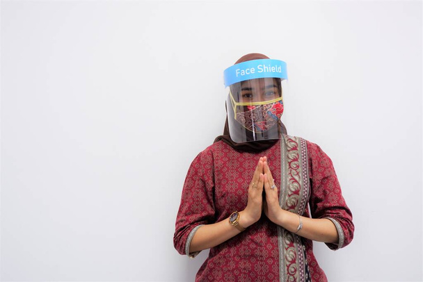 Nuori kaunis aasialainen nainen antaa lämpimän tervehdyksen vieraalle ja yllään naamio ja kasvot hänen turvallisuutensa covid-19-viruksesta - Valokuva, kuva