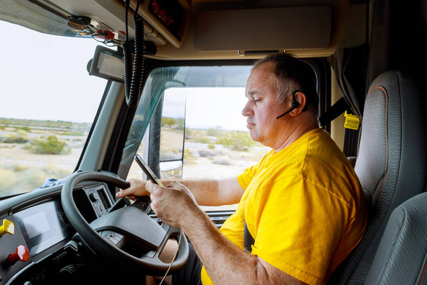 Conductor en cabina en la carretera del teléfono inteligente en la mano del hombre sentado detrás del volante de un gran vehículo de camión moderno
 - Foto, imagen