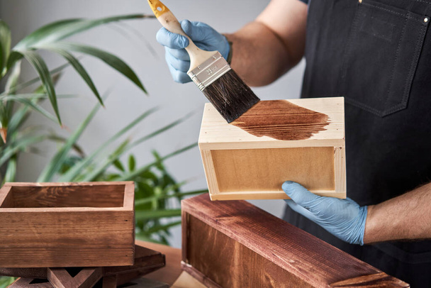 Homem carpinteiro envernizando caixa de madeira para flores com escova em seu pequeno negócio oficina de madeira. Em seu trabalho, você usa manchas ou conservantes de madeira para mostrar o padrão de madeira
. - Foto, Imagem