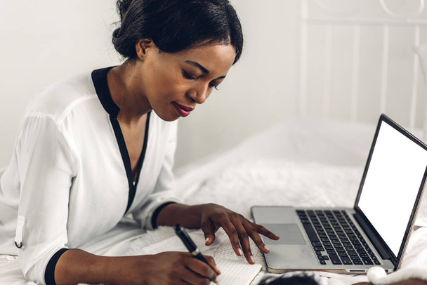 Portrait de sourire femme noire afro-américaine heureuse se détendre en utilisant la technologie de l'ordinateur portable tout en étant assis sur le lit.Jeune fille africaine créative travaillant à la maison. - Photo, image