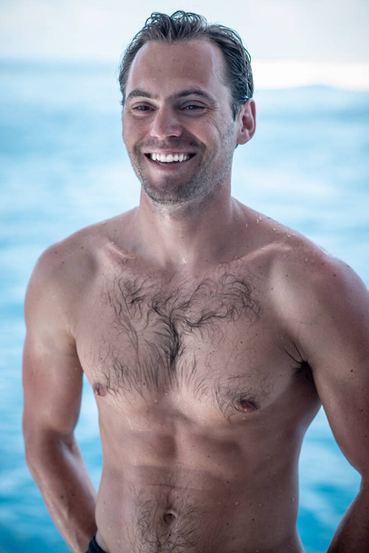 Portrait of handsome happy, sexy man with white teeth smile and wet body, surfer  and blue ocean on background - Zdjęcie, obraz