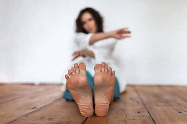 Women's bare feet in the foreground.The girl is sitting on a wooden floor on a white background - Foto, immagini