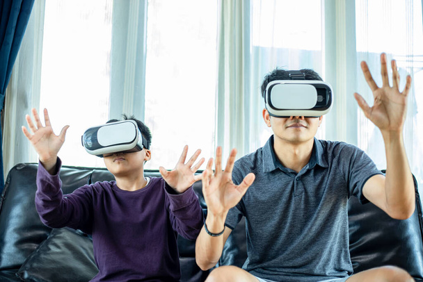 Asiatico padre e figlio piace giocare ai videogiochi insieme con joystick video e occhiali di realtà virtuale con eccitante e molto divertente in soggiorno a casa - Foto, immagini