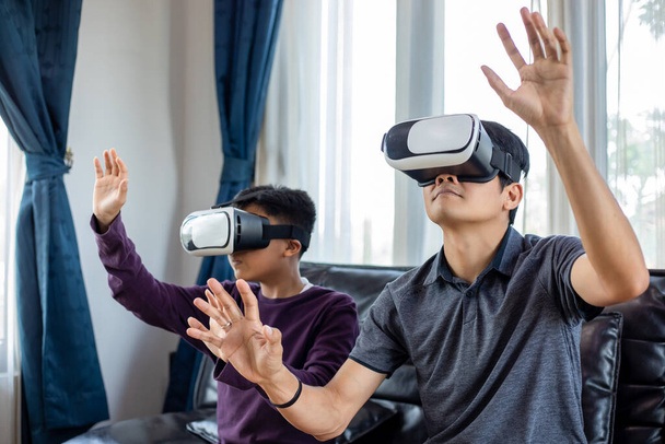 Aasialainen isä ja poika nauttivat videopelien pelaamisesta yhdessä videopelien ohjaimen ja virtuaalitodellisuuden lasien kanssa jännittävällä ja erittäin hauskalla kotona olohuoneessa - Valokuva, kuva