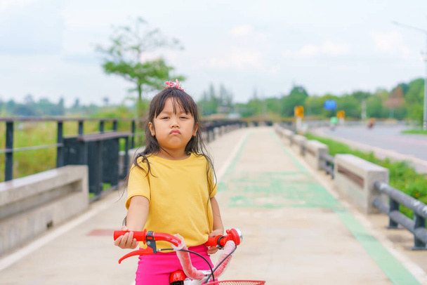 Little child girl to ride bicycle in outdoor sports ground on sunny summer day. Active leisure and outdoor sport for children. - Foto, Bild