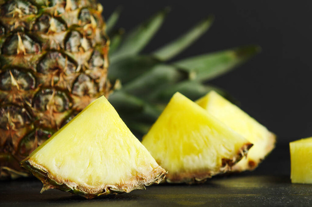 Pineapple and pineapple slices on black background. Delicious, juicy, dietary, summer fruit - Фото, изображение