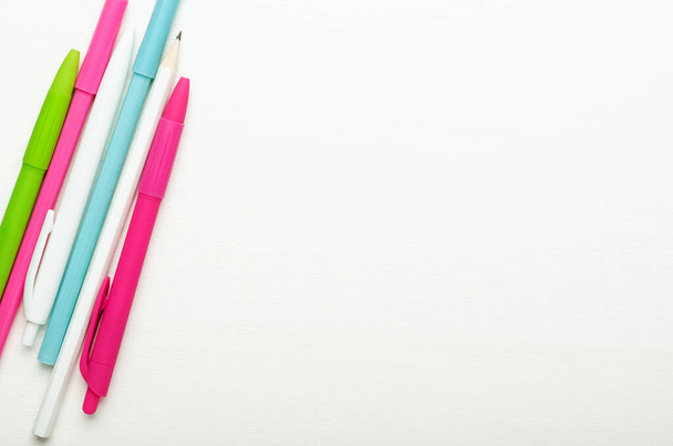 Kolorowe jasnoszkolne długopisy i ołówki dla dzieci na białym drewnianym tle, biurko szkolne. Przestrzeń kopiowania, widok z góry, układanie płaskie - Zdjęcie, obraz