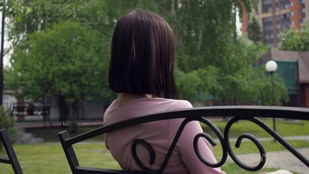 Elegante jonge brunette ontspannen op bank in park - Video