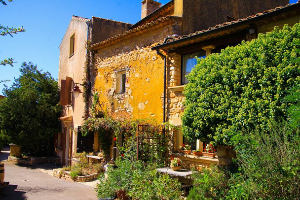 Roussillon en Provence, France - October 2. 2019: View on rural yellow stone house with trees, flower pots and trees on sunny day - Φωτογραφία, εικόνα