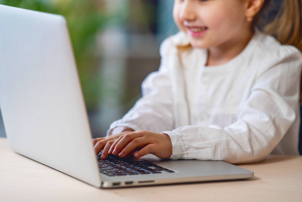 Close-up of little girl's hands, using laptop to learn from home. child smiles happily and gets knowledge remotely. digital concept remote e-learning , during epidemic, quarantines and self-isolation. - Fotoğraf, Görsel