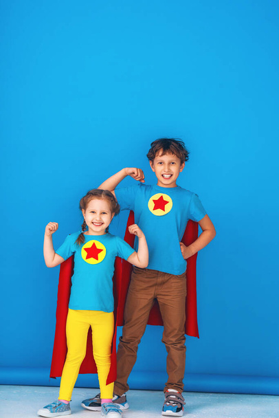 Funny little kids super hero power in red raincoats and mask. The concept of a superhero. Studio portrait over blue background. a team of heroes ready to fight. strong little children - Fotó, kép