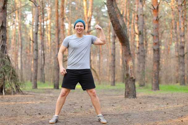 Jeune homme faisant de l'exercice dans le parc du matin et montrant biceps. - Photo, image