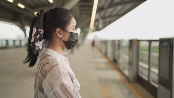 Азиатская молодая женщина в черной маске стоит на платформе станции метро железнодорожной станции, covid19 пандемии, дама стоять в одиночестве внутри неба железнодорожного вокзала Новая нормальная жизнь, ожидание в очереди, общественный транспорт, дневной свет - Кадры, видео