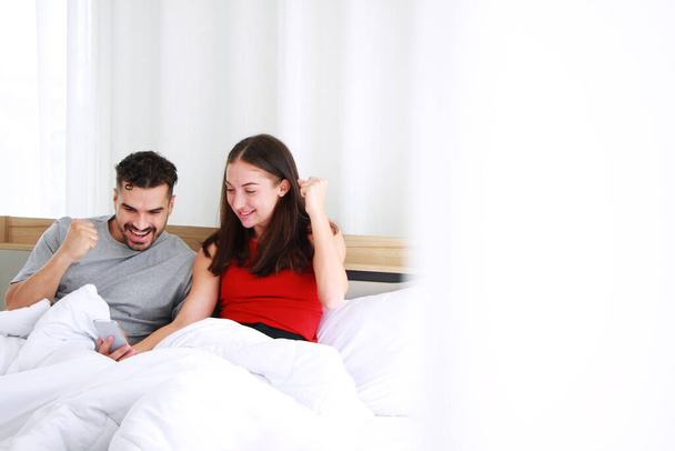 Sonriente pareja caucásica amor relajarse y trabajar en línea para los negocios en el ordenador portátil en la tecnología de redes sociales en el dormitorio. Trabajo desde el hogar y el estilo de vida familiar en vacaciones Concepto
. - Foto, Imagen