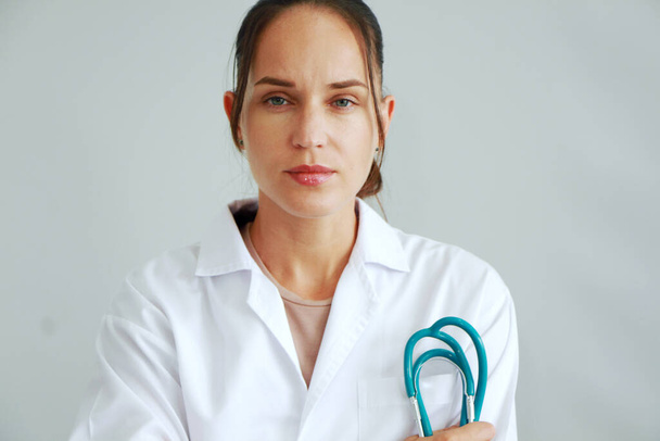 Умная кавказская врач женщина в форме халата со стетоскопом улыбается портрет на белом фоне стены
. - Фото, изображение