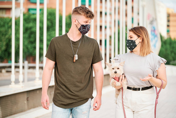 可愛いです女性とハンサムな男の顔マスクを身に着けている彼らの犬と散歩-コロナウイルスの概念 - 写真・画像